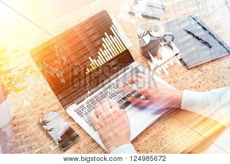 Businessman typing on laptop glass of water smartphone and notebooks aside. Graphs and diagrams. Only hands seen. Double exposure. Concept of work.