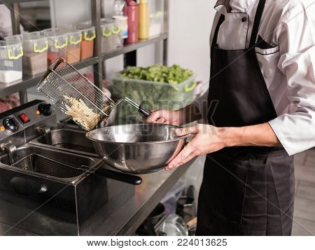 French fries - best junk food ever. Cook preparing fast food in the restaurant kitchen. Unhealthy and unbalanced eating concept