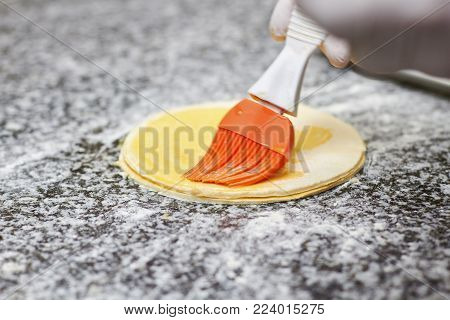 Greasing round dough close up. Round dough for a fancy cake greasing by red brush.