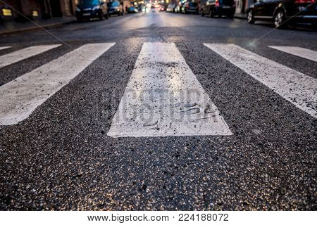 City street with blurred cars and wet asphalt closeup of a white pedestrian cross over