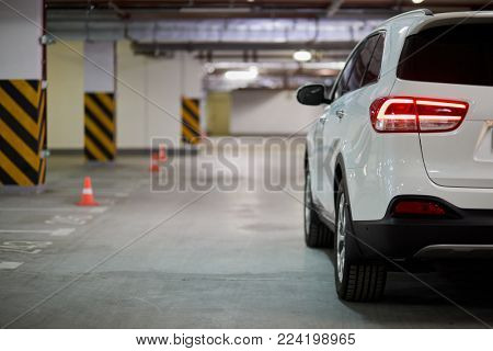 Driver side of white modern car at underground parking, side rear view.