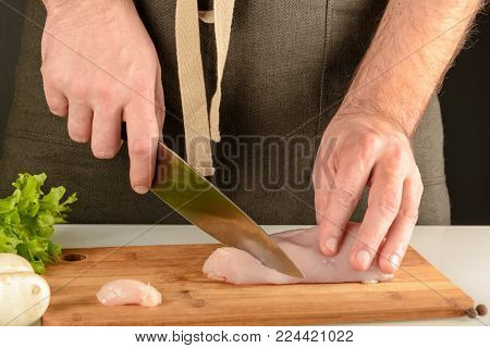 Preparation of healthy food.A man in an apron is cutting meat on a wooden board. Chicken making.
