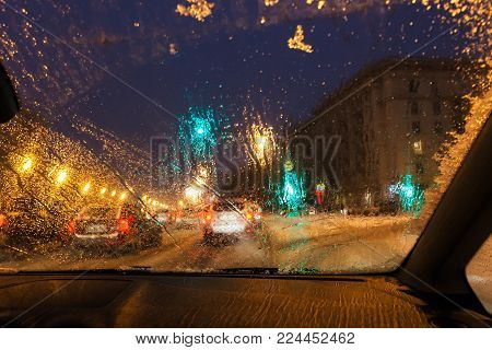 driving in night snowfall in Moscow - defocused background with view from melting snow on car windshield in evening