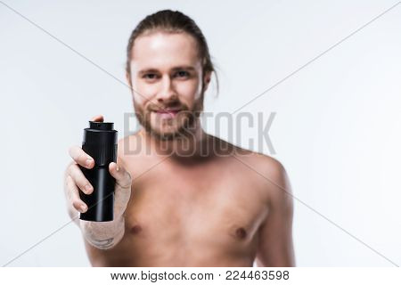 Cheerful young man holding deodorant spray in outstretched hand