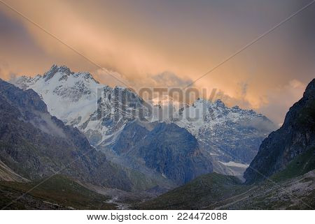 Colorfull sunset sky, clouds and mountains in high valley. Huge icy peaks.