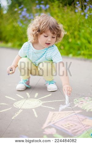 Sunny And Warm Summer Days And Happy Chilhood. Cute Little Girl Drawing With Chalk Crayons Outdoors.