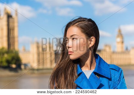 Travel London woman at Westminster, Big Ben, famous holiday destination. Autumn travel lifestyle. Asian girl portrait wearing blue trench coat in urban city.