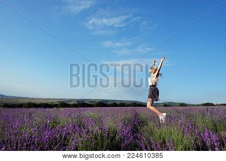 Girl in a lavYoung beautiful blond girl walking, jumping and laughing in the summer morning sunny lavender field. A pink blouse and sunglasses are dressed in a gray skirt hat. South of Russia, field, lavender, freedom and happiness.ender field in summer