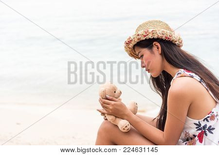 lone Asian girl long hair dressed in white with flowers and hats hugging bear beside beach thinking Dear man of the beloved far away. Women sit and wait for lovers on Valentine's Day.