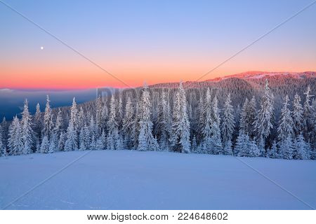 Landscape with high mountains covered with snow. Interesting frozen texture. Beautiful winter sunrise with orange blue sky. Place for tourists. Christmas story.