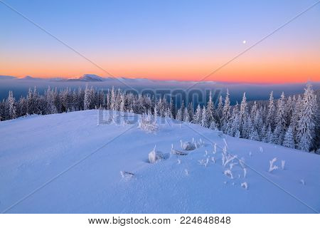Landscape with high mountains covered with snow. Interesting frozen texture. Beautiful winter sunrise with orange blue sky. Place for tourists. Christmas story.