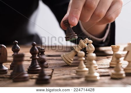 Close-up Of A Businessperson Checkmating King Chess Piece With Rook On Wooden Desk