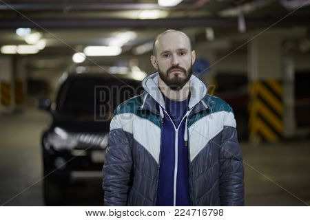 Half-length portrait of bearded man standing at underground parking.