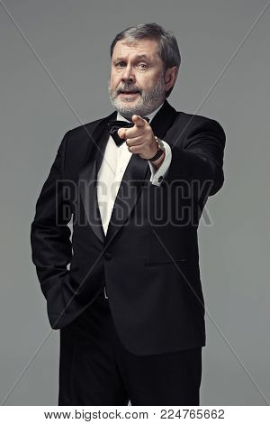 The senior businessman standing against gray studio background and pointing to camera. The concept of choice