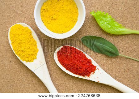 Cooking hot spicy meal. Dry red pepper and curcuma in wooden spoons and bowl with fresh herbs and on a corkwood background with copy space, top view