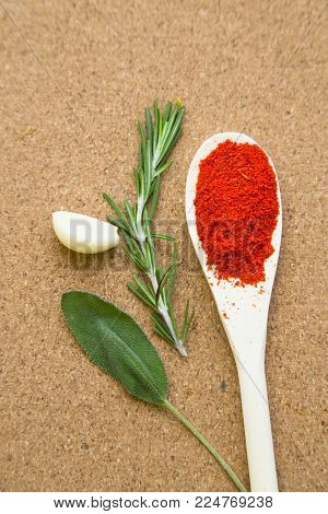 Cooking hot spicy meal. A wooden spoon with dry chili pepper, fresh rosemary, a salvia leaf and a garlci cloves, corkwood background, top view