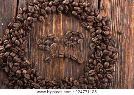 Smile shaped of roasted coffee beans on white wood background.