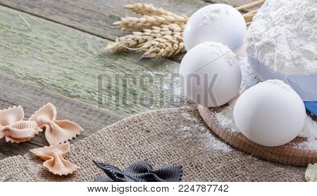 Spike of wheat, pasta, eggs and flour on a wooden background, with space for text.