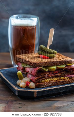 Delicious huge pastrami sandwich with beer and pickle on wooden board