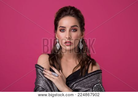 Beautiful young girl in fine earings wearing a silver jacket cropped portrait against pink background