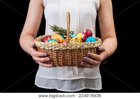Woman holding basket with colorful easter eggs. Hands holding easter basket on black background