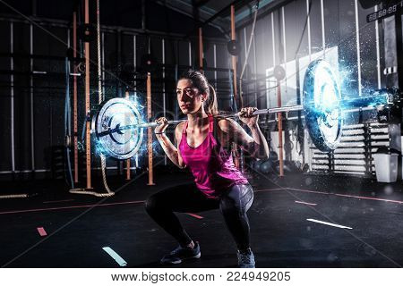 Determined athletic girl works out at the gym with a with blue energy effects