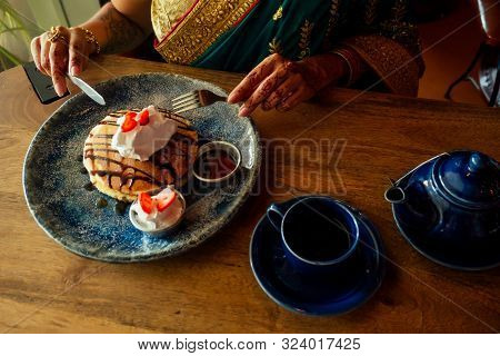Portrait Of A Indian Woman In Green Sari And Gold Jeweler Looking At Pancakes With Whipped Cream And