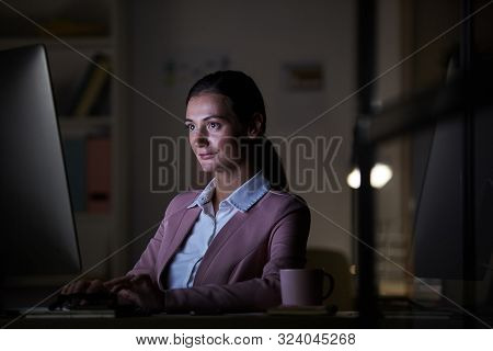 Young Confident Businesswoman Sitting At The Table In Front Of Computer Monitor And Typing On Comput
