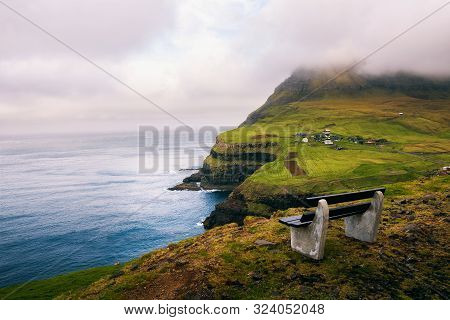 Bench Above The Village Of Gasadalur With Views Over Beautiful Faroese Scenery And Atlantic Ocean On