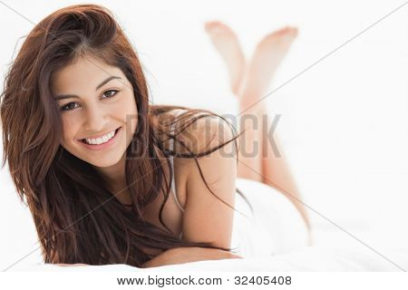 En kvinde, der smiler med armene krydset på sengen, hendes ben rejst og krydsede.