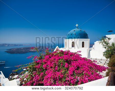 Majestic View Of Nikolaus Monastery With Domed Church And Pink Flowers On Seashore Of Santorini Isla