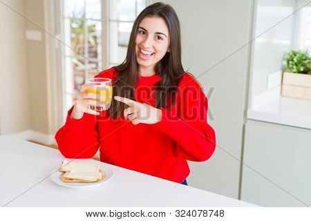 Beautiful young woman eating toasts and orange juice for snack or breakfast very happy pointing with hand and finger