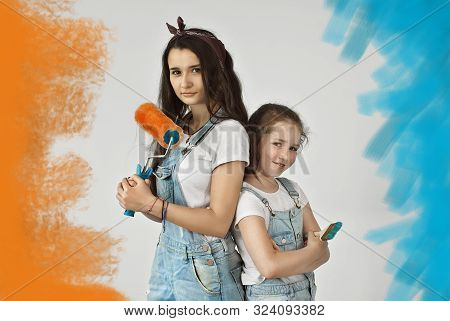 The Girls Paint The Walls. Friendly Collaboration Between The Two Sisters. Teens In Blue Overalls Ma