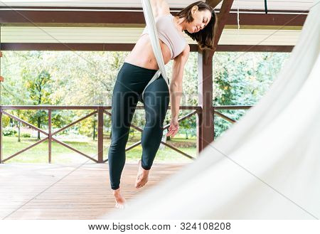 Pretty Young Woman Practising Anti-gravity Fly Yoga In White Hammock. Stretching Exercises Outdoors