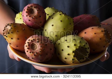 Female Hands Hold A Plate With Ripe Fresh Fruits Of Prickly Pear On A Gray Background, Low Key, Sele