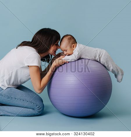 Happy Mother Doing Exercises With Her Infant Child Baby On Purple Yoga Ball
