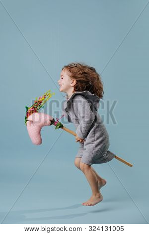 Little Girl Is Hopping On A Hobbyhorse, Hovering In The Air Over Blue Background