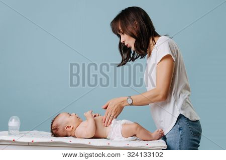 Mother Palping Babys Stomach On Table While Talking To Him Over Blue Background