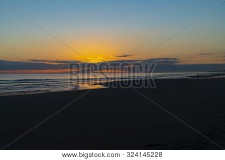 Oceanbeach As Sun Is On Horizon Creating Golden Glow Across Sea To Beach Still In Dark Of Morning.