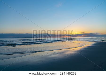 Oceanbeach As Sun Is On Horizon Creating Golden Glow Across Sea To Beach Still In Dark Of Morning.
