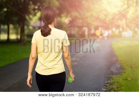 Woman Exercise Walking In The Park With Bottle Water At Sunrise.