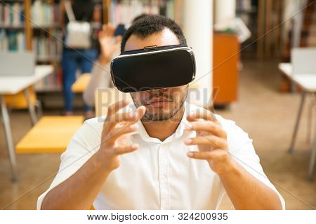 Excited Male Student Using Vr Simulator During Class. Latin Man In Virtual Reality Glasses, Sitting 