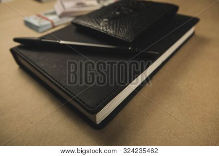 A Black Notebook , A Pen And Dollar Cash Banknotes On Wooden Background - Concept Of Financial Manag