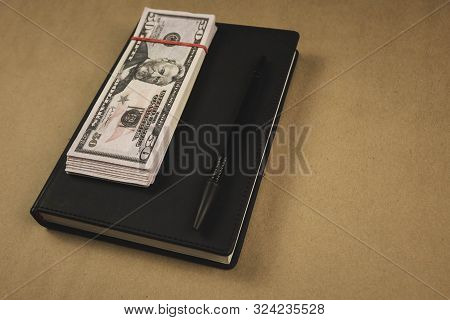 A Black Notebook , A Pen And Dollar Cash Banknotes On Wooden Background - Concept Of Financial Manag