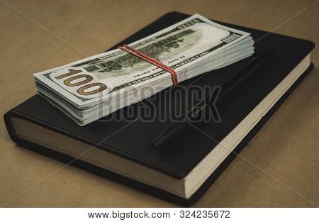 A Black Notebook , A Pen And Dollar Cash Banknotes On Wooden Background - Concept Of Financial Manag