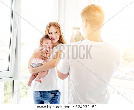 Mother and baby posing for father taking photo indoors