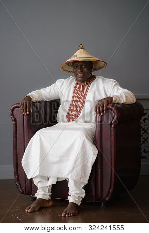 Handsome African Man In Traditional White Dress And Fulani Hat On Gray Background