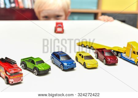 Young Boy Playing Child Is Peeking Over The Table Whilst Playing With Cars