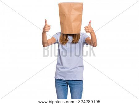 Portrait of teen girl with paper bag over head making thumb up gesture. Teenager cover head with bag showing success sign isolated on white. Child pulling paper bag over head.