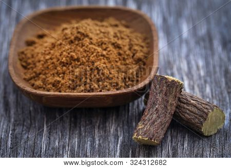 Liquorice Stick And Ground Herbs In Wooden Bowl On Textured Surface